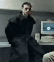 a man in a black coat is sitting in front of a computer monitor