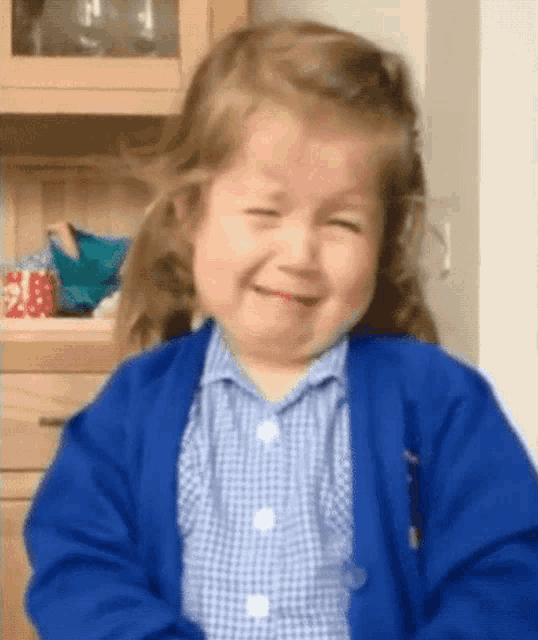 a little girl wearing a blue cardigan and a plaid shirt is crying .