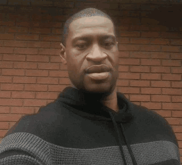 a man in a black and grey sweater is standing in front of a brick wall and taking a selfie .