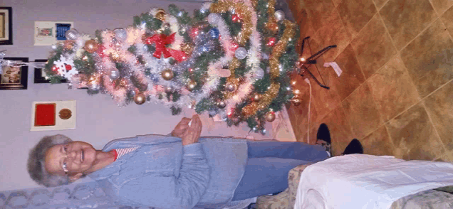 an elderly woman stands in front of a christmas tree that is decorated in pink and silver