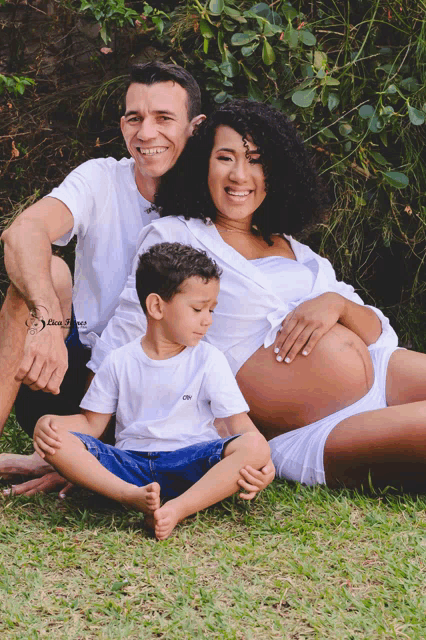 a pregnant woman sits in the grass with her husband and son and a watermark that says don gomez