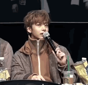 a young man is holding a microphone in his mouth while sitting at a table with a starbucks cup in front of him