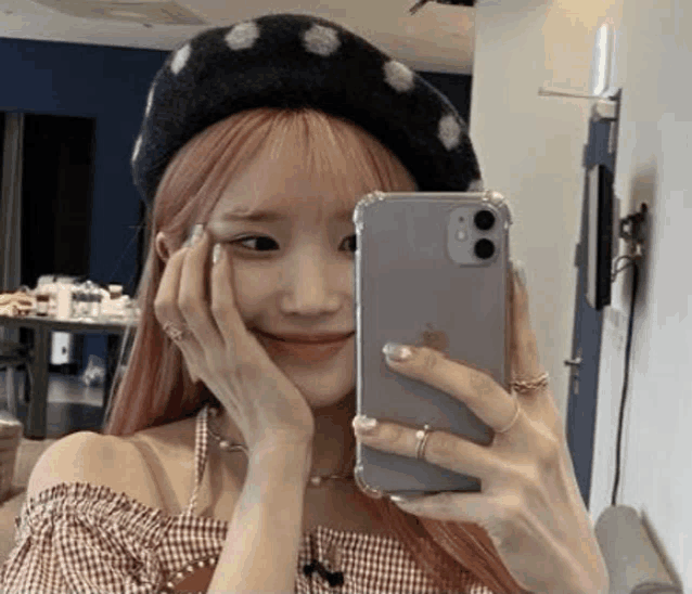 a woman wearing a beret is taking a selfie with her phone in a mirror .