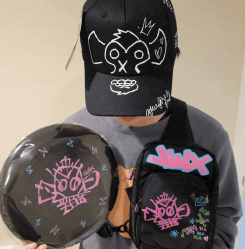 a person wearing a black hat with a monkey on it holds a black frisbee and a black bag