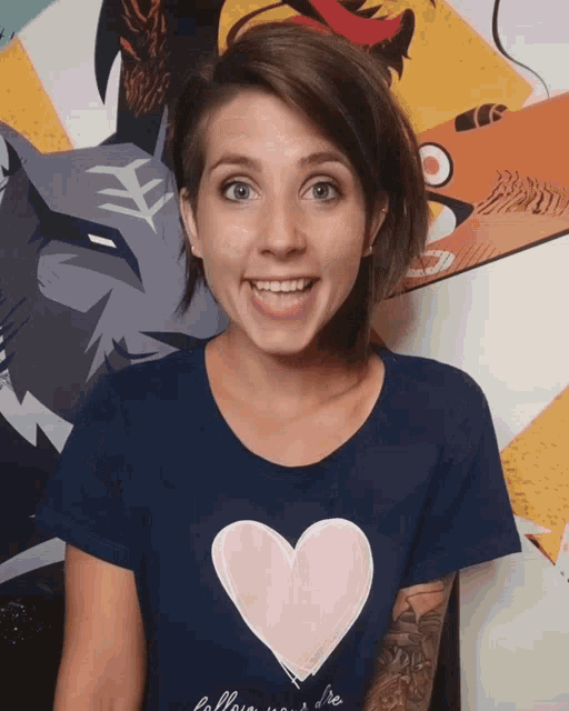 a woman wearing a blue shirt with a pink heart on it is smiling