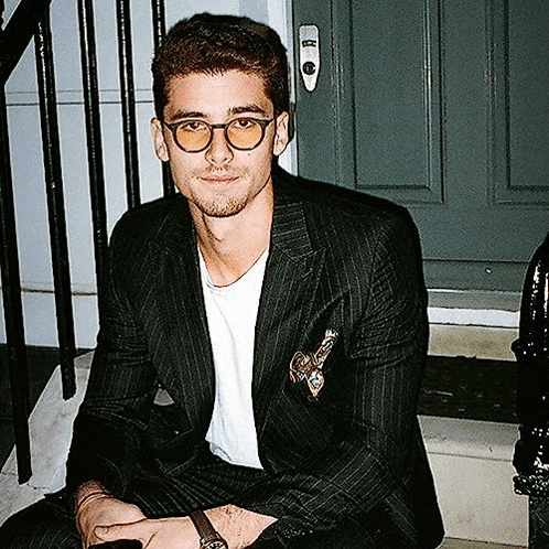 a young man in a suit and glasses is sitting on a set of stairs .