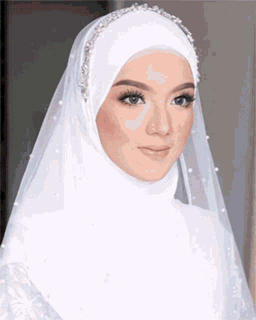 a woman wearing a white hijab and veil with pearls on it .