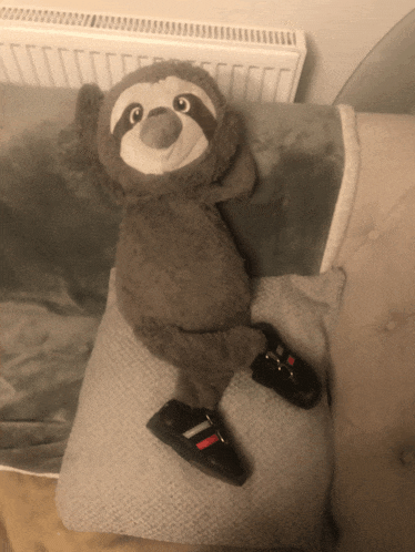 a stuffed sloth laying on a pillow with a pair of black shoes on it