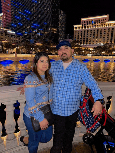 a man and a woman are posing for a photo in front of a body of water