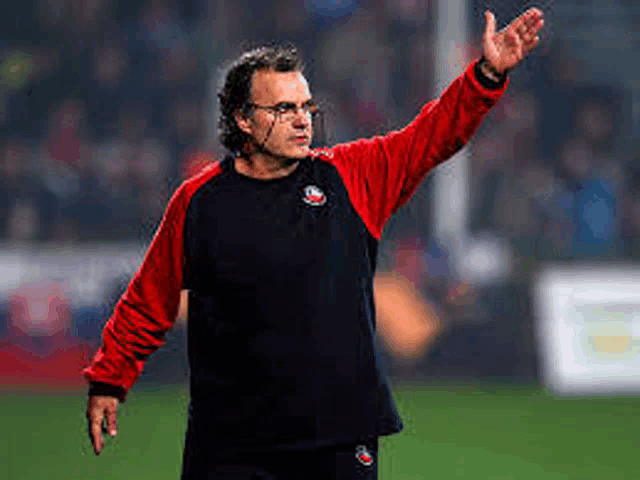 a man wearing glasses and a black and red shirt is standing on a soccer field