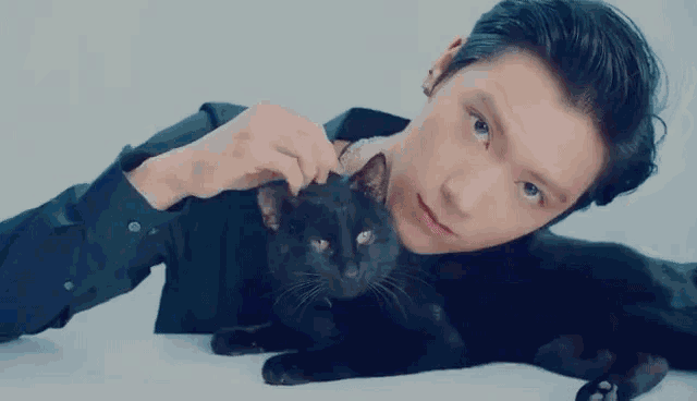 a man in a black shirt is petting a black cat on a table .