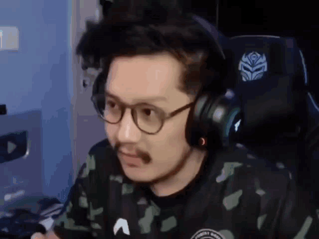 a man with a mustache and glasses is wearing headphones and a camo shirt .