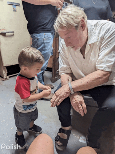 a little boy in a red white and blue shirt is standing next to a man in a white shirt