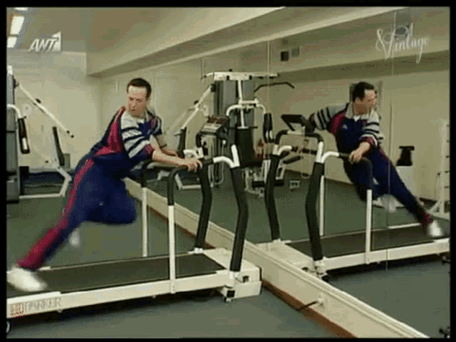 a man is running on a treadmill in front of a mirror with ant written on the wall behind him