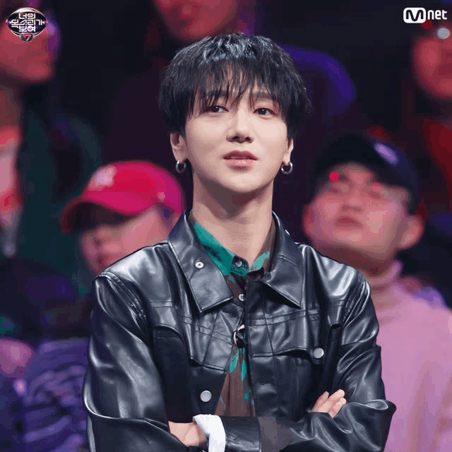 a man in a leather jacket stands in front of a crowd with the word mnet on the bottom left