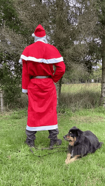 a man dressed as santa claus stands next to a dog on a leash