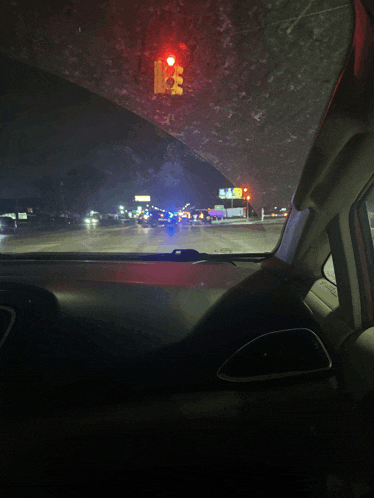 a car is driving down a street at night with a red traffic light in the background