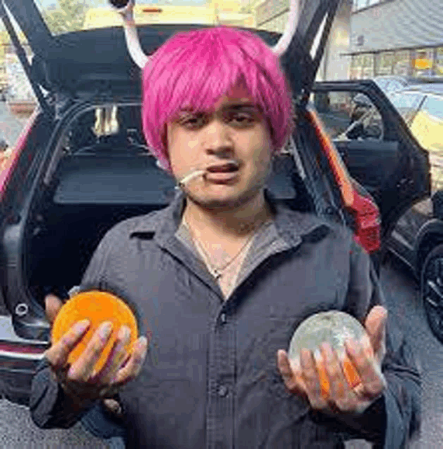 a man with pink hair and horns is holding an orange and a cantaloupe .