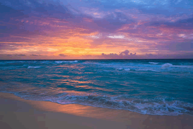 a sunset over a beach with waves crashing on the sand