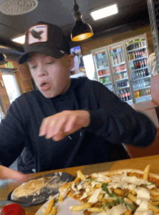 a young boy wearing a black hat is eating a pizza with french fries