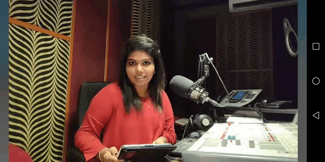 a woman in a red shirt is sitting in front of a microphone in a radio studio