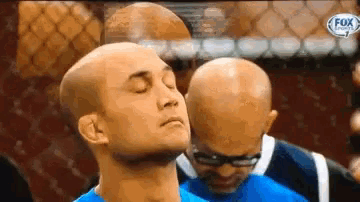 a bald man with his eyes closed is standing next to a referee .