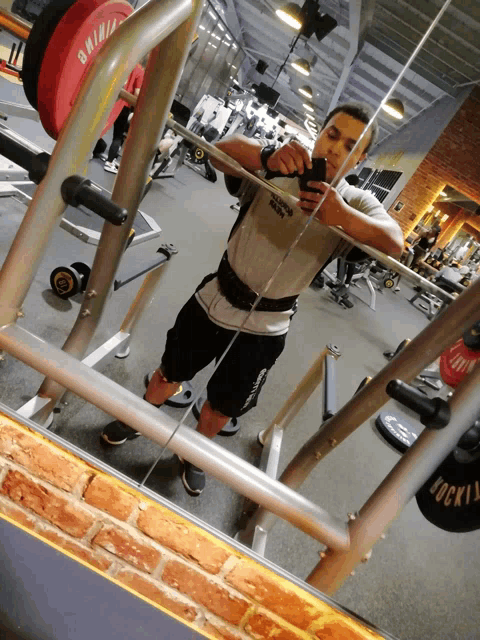 a man taking a picture of himself in a gym with a barbell that says gainz