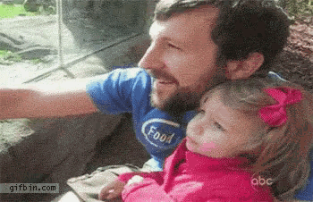 a man is holding a little girl in his arms while they look out a window at a zoo .