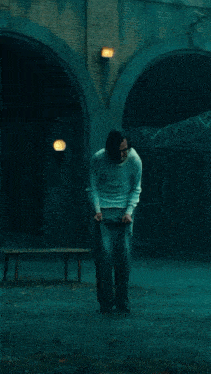 a man in a white sweater and blue pants is standing in front of a building in a dark room .