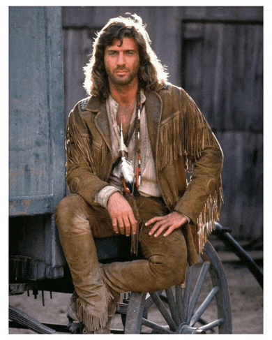 a man in a fringed leather jacket sits on a wagon wheel