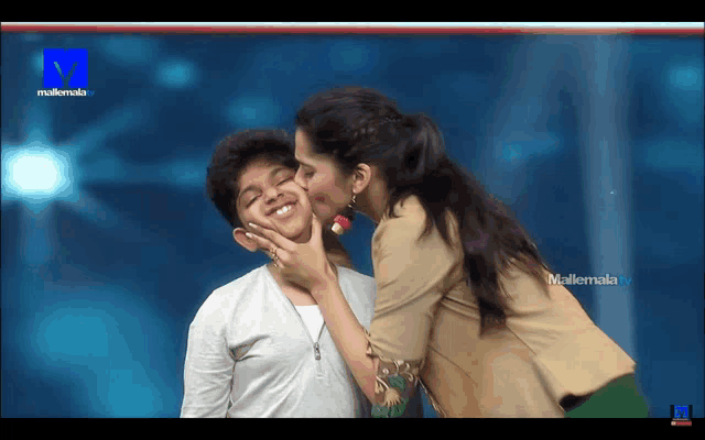 a woman kisses a young boy on the cheek in front of a screen that says mallemala tv