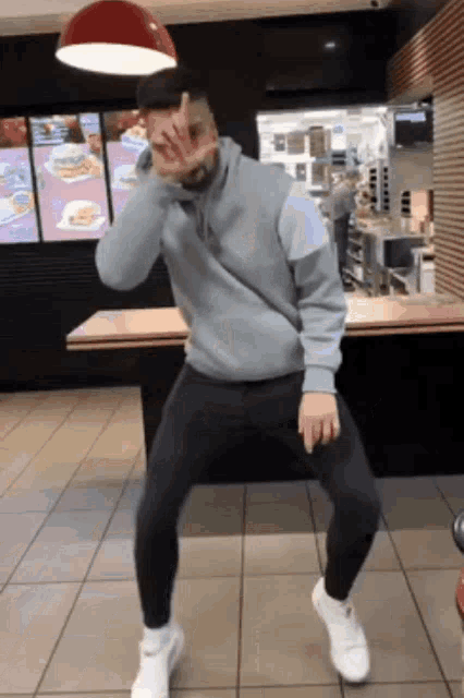a man in a gray sweatshirt is dancing in a restaurant