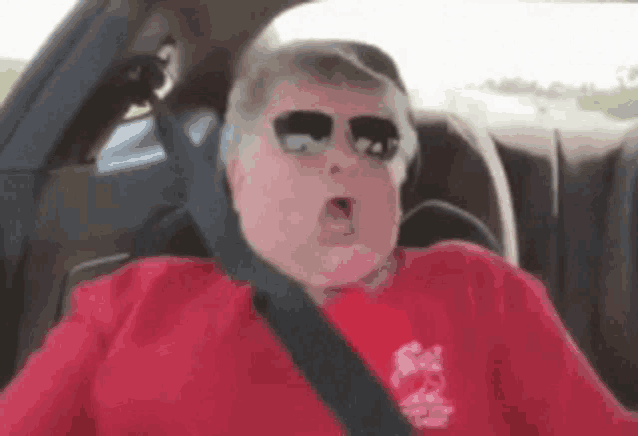 a man wearing sunglasses and a red shirt is sitting in a car .