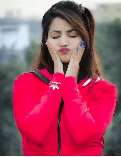 a woman wearing a pink adidas sweatshirt holds her hands to her face