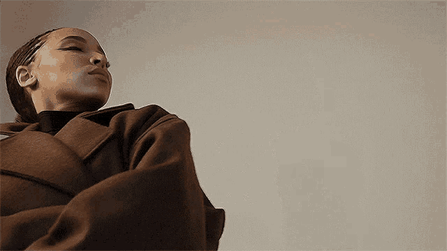 a woman in a brown coat and black turtleneck is looking up