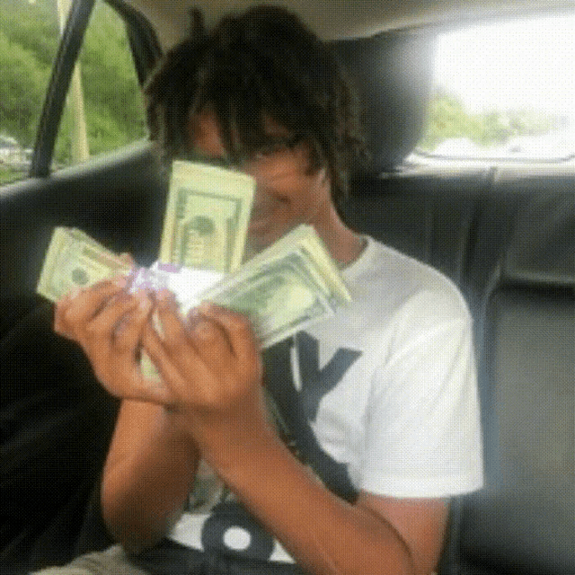 a man in a white shirt with the letter y on it is holding a bunch of money in front of his face