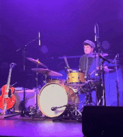 a man playing drums on stage with a guitar in the background