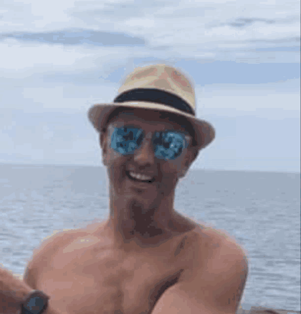 a shirtless man wearing a hat and sunglasses is taking a selfie in the ocean .