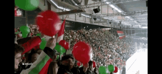 a crowd of people holding red and green balloons in a stadium that says " aktuell " on the bottom