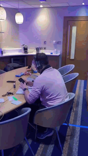 a man wearing headphones sits at a table looking at his cell phone