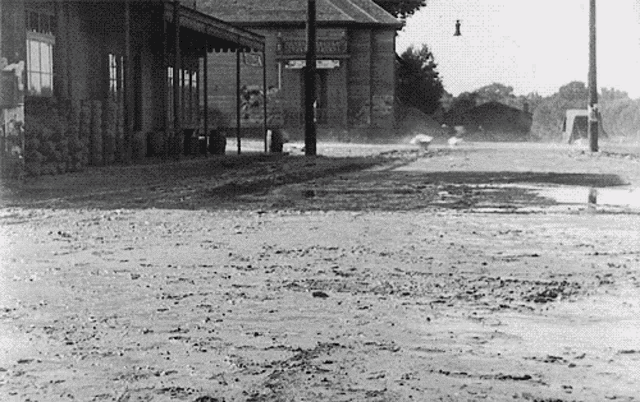 a black and white photo of a muddy street in front of a building that says ' warehouse ' on the front