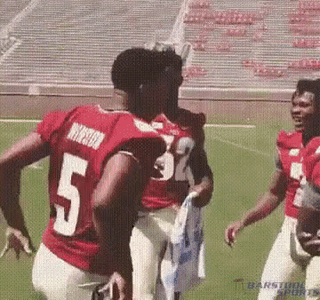 a group of football players are standing on a field . one of the players is wearing a number 5 jersey .