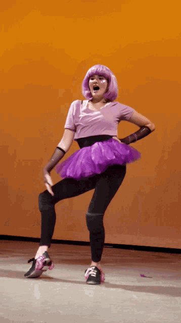 a woman wearing a purple tutu and roller skates stands on a stage