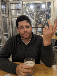 a man sitting at a table with a glass of beer in front of a sign that says poe street