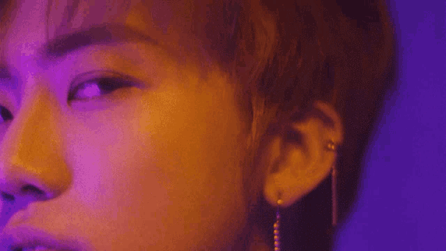 a close up of a man 's face with a purple background and earrings .