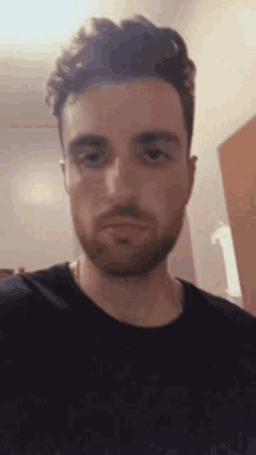 a man with a beard is wearing a black shirt and looking at the camera