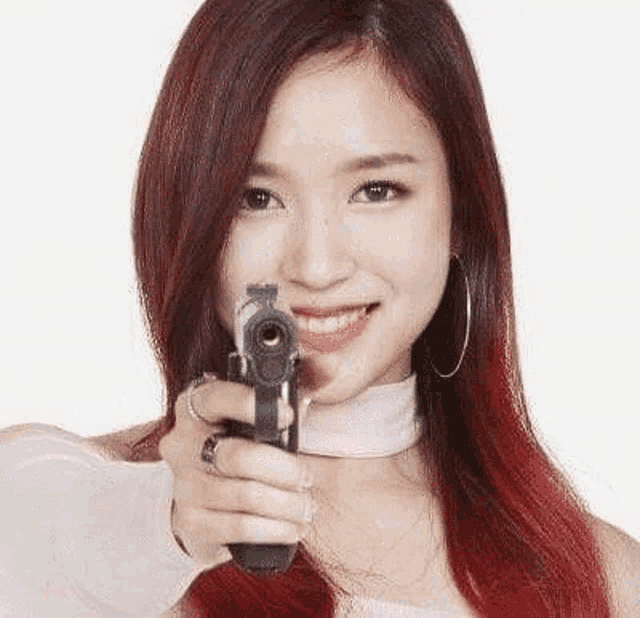 a woman with red hair is holding a gun in front of her face and smiling .