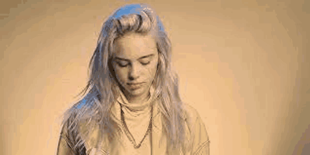 billie eilish is wearing a yellow sweater and a necklace while looking down .