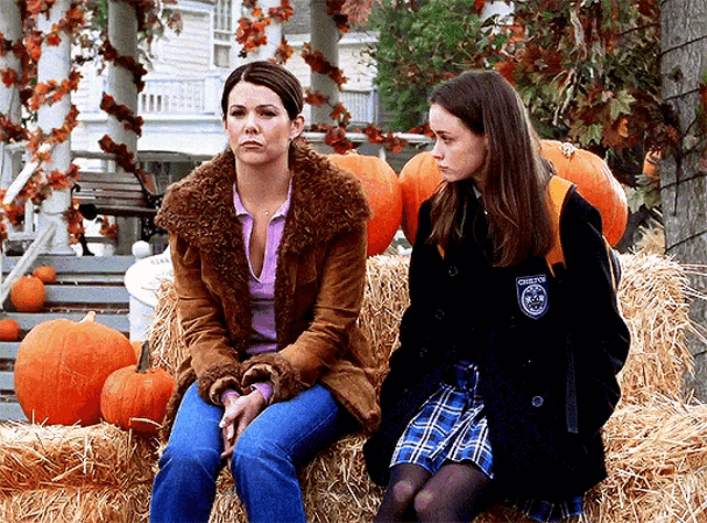 two women are sitting on a bale of hay with pumpkins in the background and one of them has a patch on her jacket that says chester