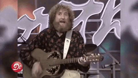 a man with a beard is playing a guitar on a stage in front of a neon sign .